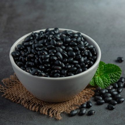 The beans are nestled in a pool of thick, dark liquid, suggesting a flavorful broth or sauce. Some beans are partially submerged, while others are fully visible on the surface. The image conveys the rich, hearty nature of black beans, a popular legume known for its distinct flavor and versatility in various culinary applications, such as soups, stews, salads, and Mexican dishes.