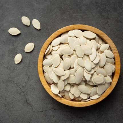 hulled sesame seeds on a white background, revealing their small, oval shape and pale beige color. The outer shells have been removed, leaving the inner seed exposed.