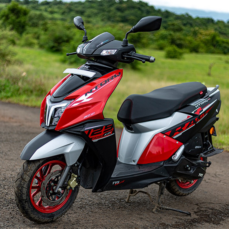 TVS NTORQ The scooter has a comfortable and ergonomic seating position, with a sporty split-seat design. It is powered by a powerful engine, with a CVT transmission, and it offers sporty performance with quick acceleration and responsive handling. The alt text highlights the scooter's dynamic appearance, performance features, and smart connectivity.